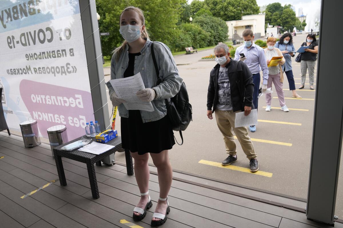 People in masks stand in a line marked by yellow tape to ensure distancing.