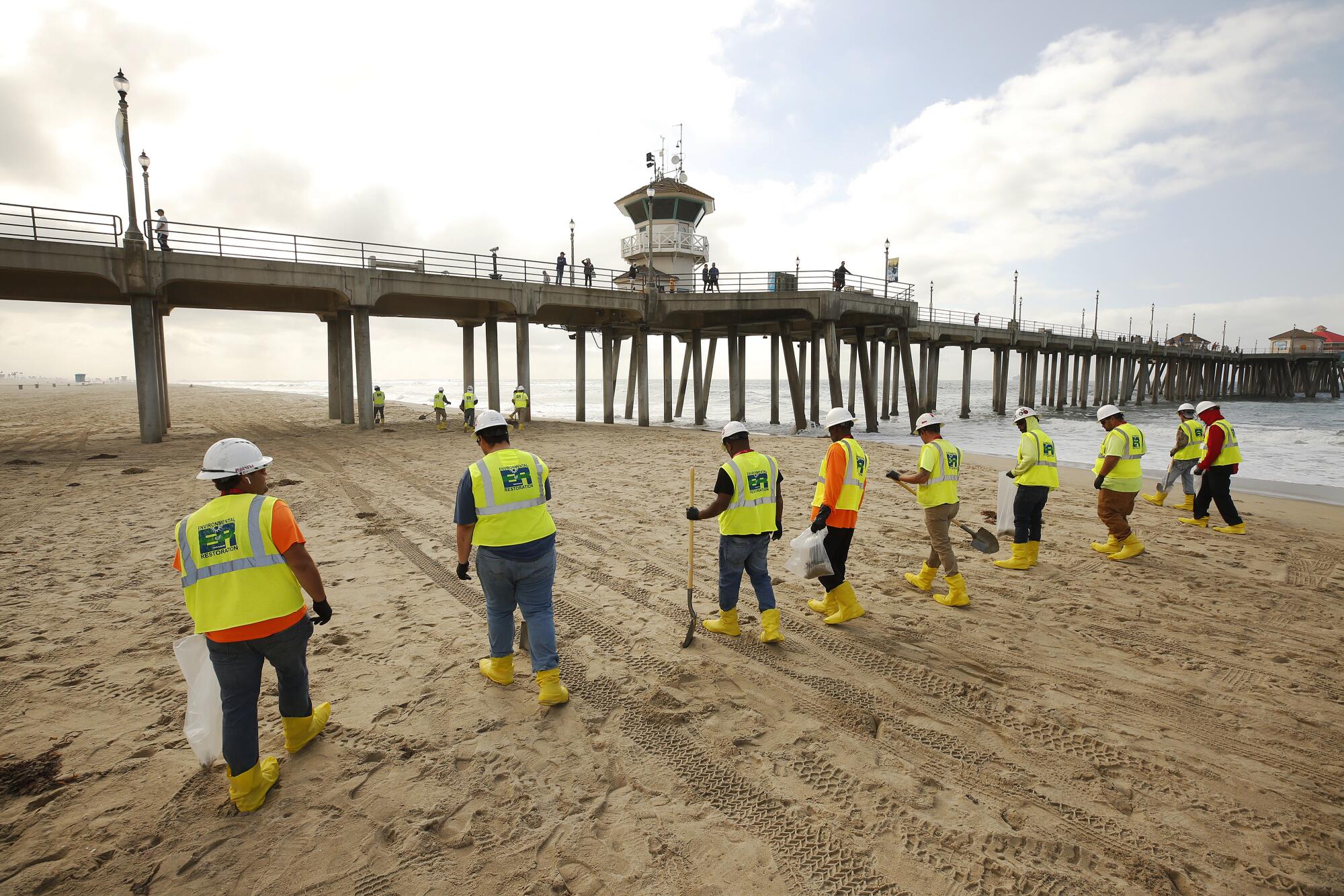 Clean-up crews continue to comb the beach under partly cloudy skies at the Huntington Beach Pier