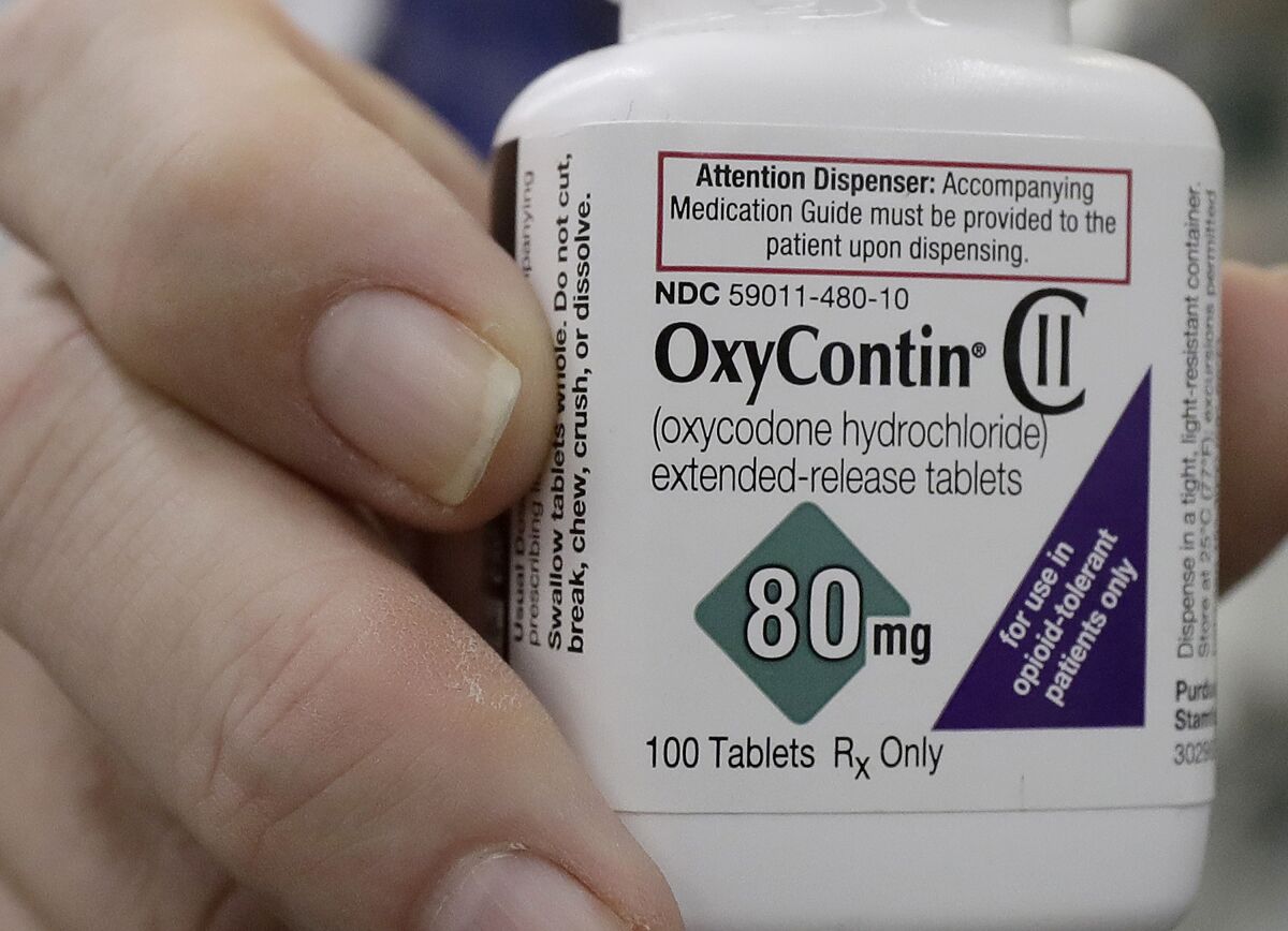 A pharmacist poses for photos holding a bottle of OxyContin.