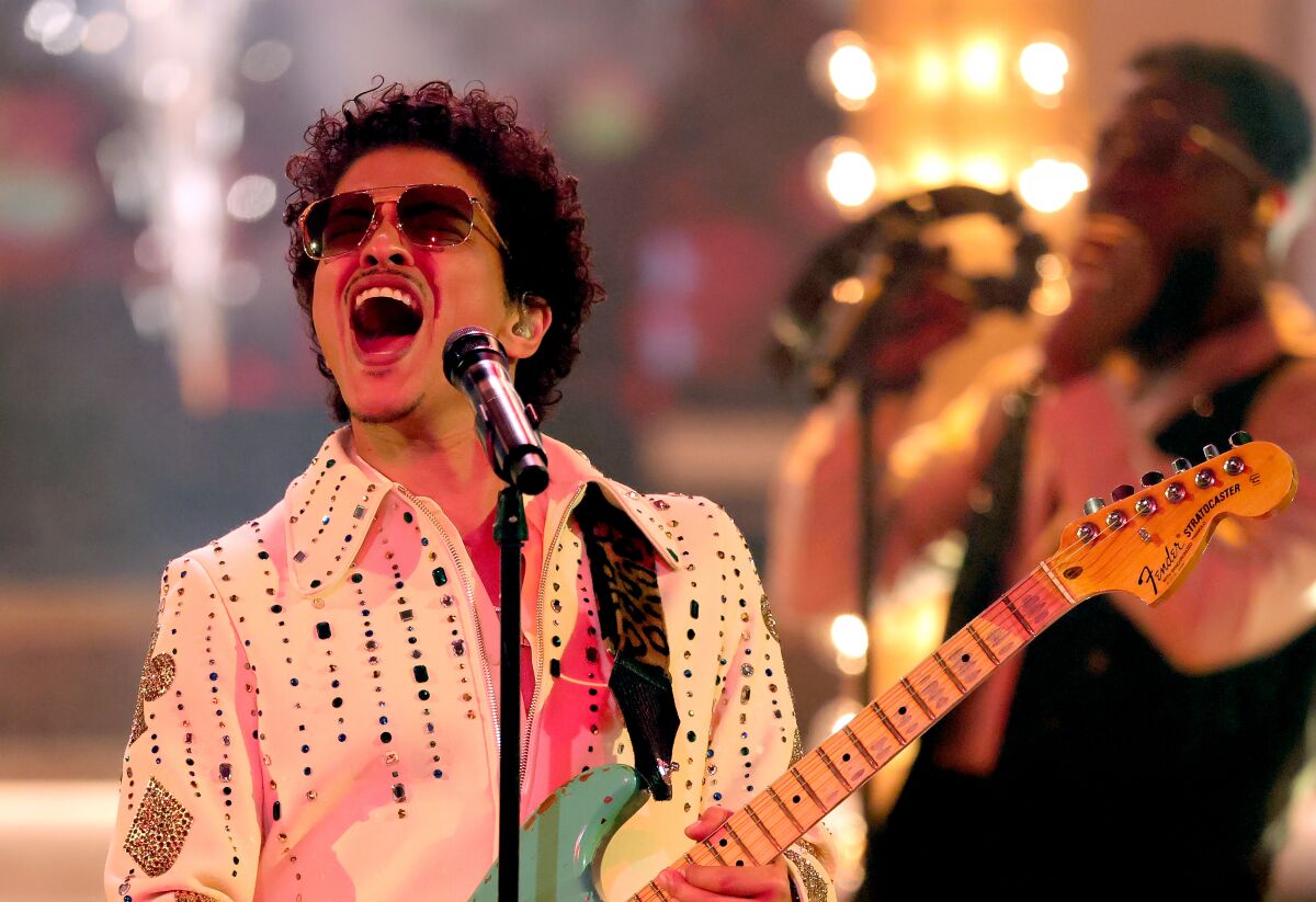A man in sunglasses singing and playing electric guitar onstage.